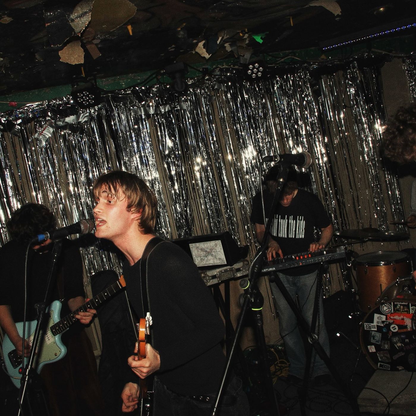 A guitarist singing in front of silver tinsel