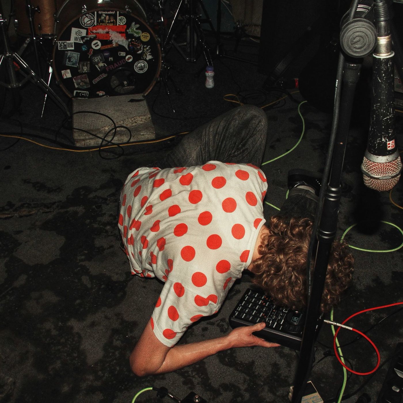 A musician in a polka-dot shirt bent double over a pedalboard