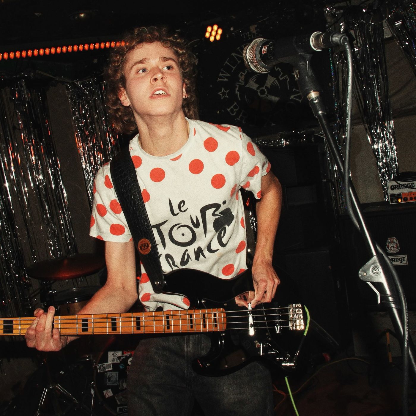 A bassist in a polka-dot shirt looking up from the stage