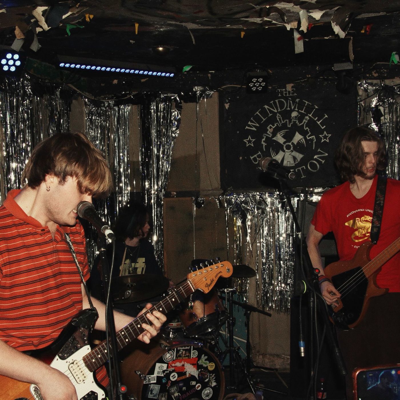 A band in striped and red shirts playing under the Windmill banner