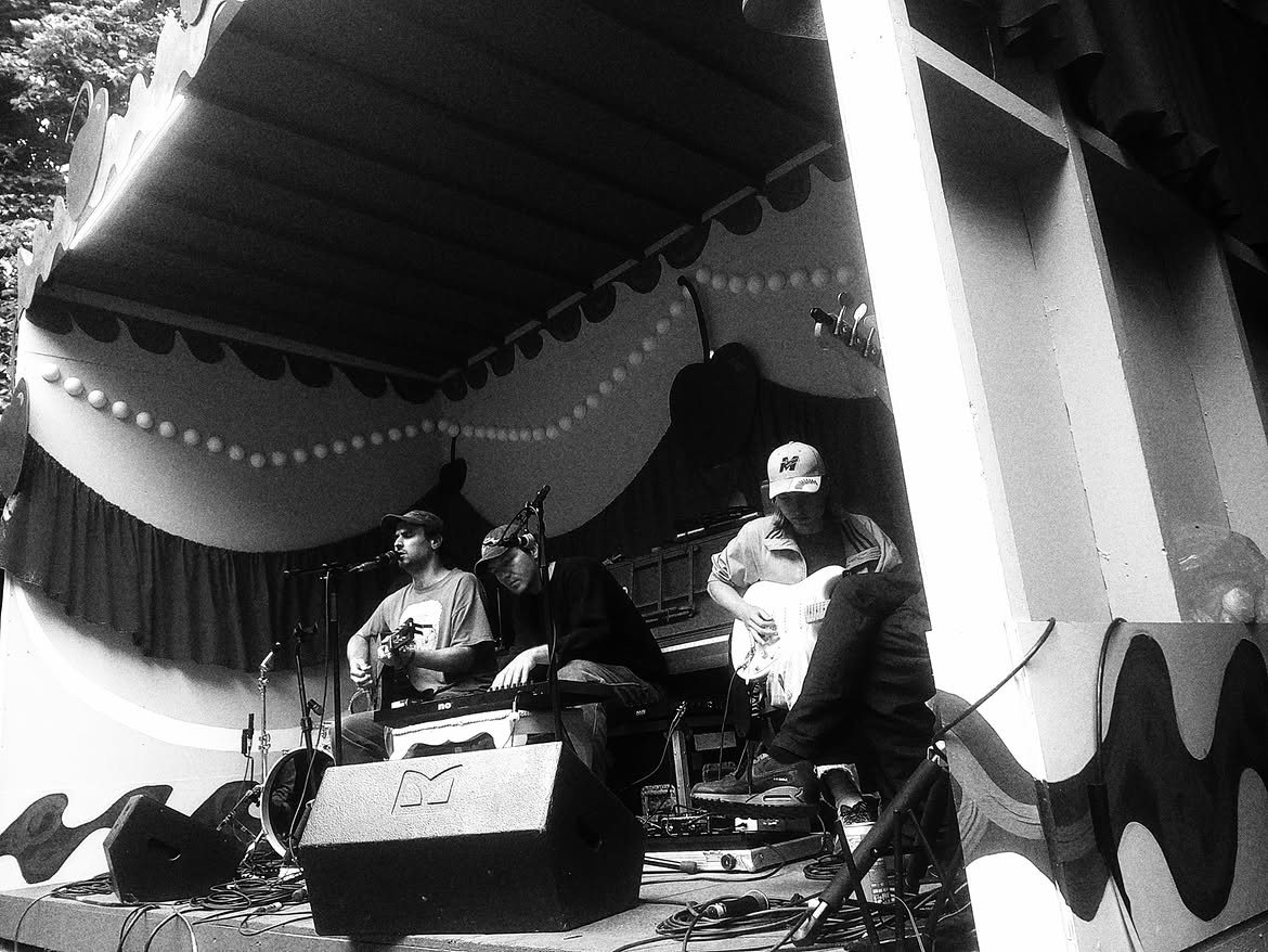 A three-piece band playing on a small painted garden stage